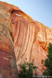 A small arch sits at the top of a colorful sandstone cliff.