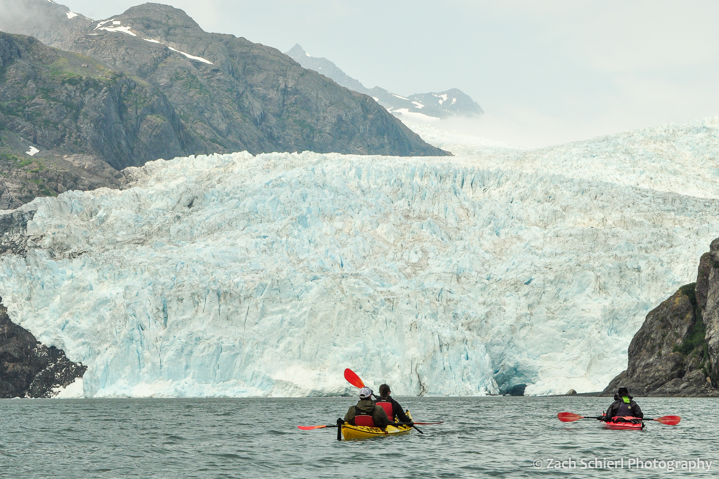 Two kayakers approach a large glacier