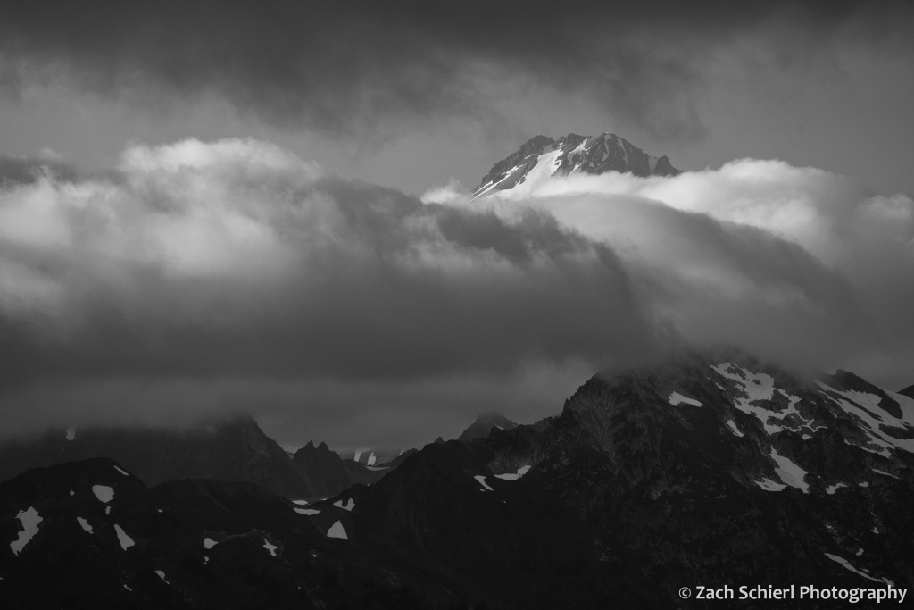 The summit of a glacier clad peak is visible through a break in the clouds
